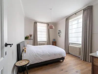 a bedroom with a bed and a table and two windows at Scenic villa in Borgloon with garden in Borgloon