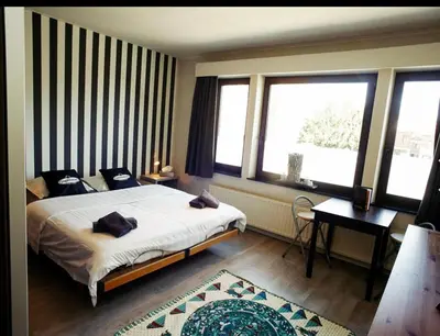 a bedroom with a bed and a desk and windows at Homestay La Montagne des Coeurs in Eigenbilzen