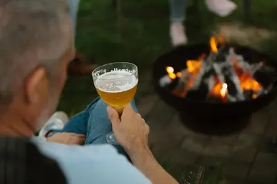 a man holding a glass of beer in front of a fire at Bij de secretaris in Kanne