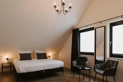 a bedroom with a bed and two chairs and a chandelier at Bij de secretaris in Kanne