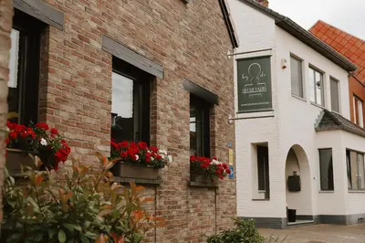 a brick building with red flowers in window boxes at Bij de secretaris in Kanne