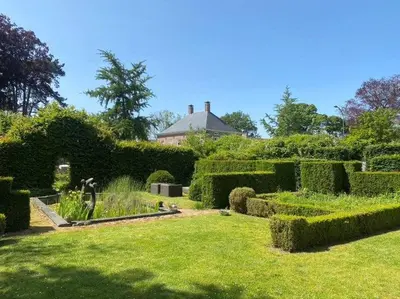 a garden with hedges and a person standing in the grass at B&B Huis Spaas in Pelt