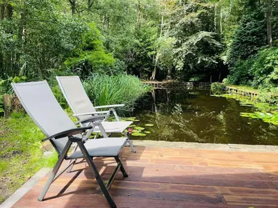 two chairs sitting on a deck next to a pond at Prachtige chalet in het bos met sauna! in Lanaken