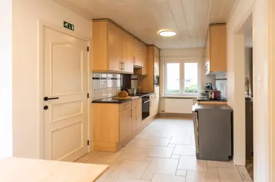 a large kitchen with wooden cabinets and a window at Aan de bosrand in Oudsbergen