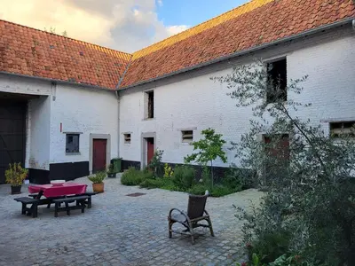 a courtyard with two white buildings with tables and chairs at Charming and cosy ART DECO house in old historic farm with private natural pool and gardens with hiking and cycling trails nearby in Sint-Truiden