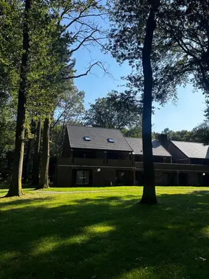 a house in a field with trees in the foreground at Bos-Chalet bij Wijers Wandelroutes, Rust & Gezinsplezier Fijnspar 6 Hengelhoef in Houthalen-Helchteren