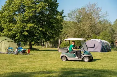 a man riding a golf cart in a field with tents at Jocomo Parc in Lanaken