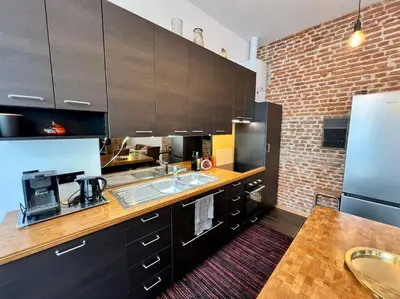 a kitchen with brown cabinets and a brick wall at Art Loft -Opéra, Saint-Lambert, Bueren in Liège