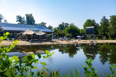 a view of a lake with a building and tents at Vakantiehuis 25 min Roermond Maasmechelen Maastricht in Kinrooi