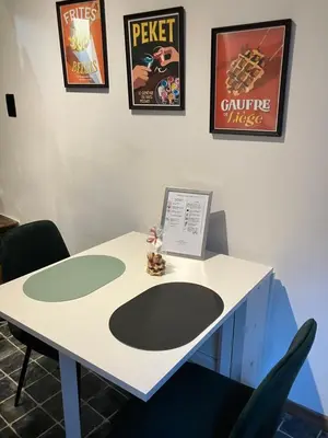 a white table with two chairs and posters on the wall at La Nano Maison de Liège in Liège