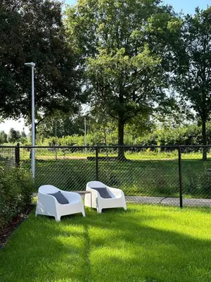 two white chairs sitting in the grass near a fence at Vakantie aan de Maas - Vakantiewoning Leenhof in Kinrooi