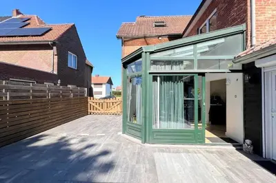 a glass house with a green door on a patio at Vakantiewoning De Merode in Lanaken