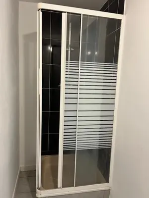 a glass shower stall with black tiles on the wall at Superbe studio à Liège in Saint-Léonard