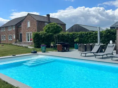 a swimming pool with two chairs and a table and a house at De Boomgaard Voeren in Voeren