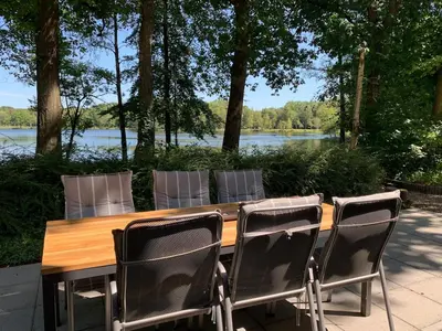 a wooden table and chairs with a view of a lake at Forest lakehouse with Breathtaking Sauna in Lanaken