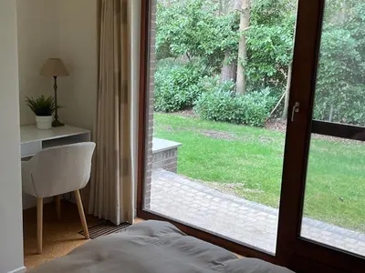a bedroom with a sliding glass door looking out at a yard at Ardilla - holiday house in an oasis of green in Heusden - Zolder
