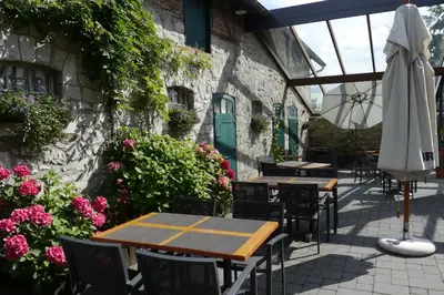 an outdoor patio with tables and an umbrella and flowers at L'Appart - New Appartement - Free Parking - Self Check-in - Terrasse in Eynatten