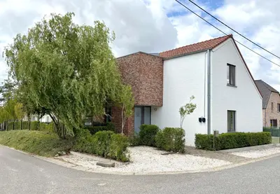 a white house with a tree on the side of a street at Vakantiewoning De Vliergeit in Limburg - Haspengouw in Hasselt