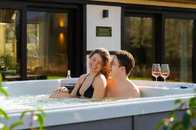two people sitting in a bath tub with wine glasses at Woodz Lodges - Unwind in nature in Heusden - Zolder