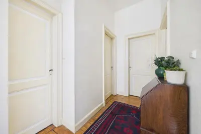 a hallway with white walls and doors and a plant on a dresser at Maison de Maître in Liège