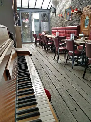 a piano in a restaurant with tables and chairs at de Twie Keuninge in Maasmechelen