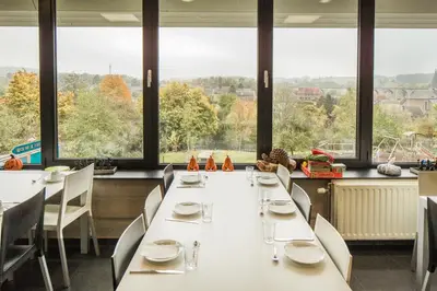 a dining room with tables and chairs and large windows at Hostel De Veurs in Sint-Martens-Voeren