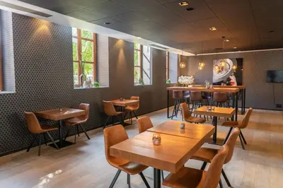 a restaurant with wooden tables and chairs and windows at Eburon Hotel in Tongeren