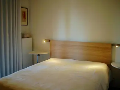 a bedroom with a white bed with a wooden headboard at Gîte Au26 côté jardin-côté cour in Liège