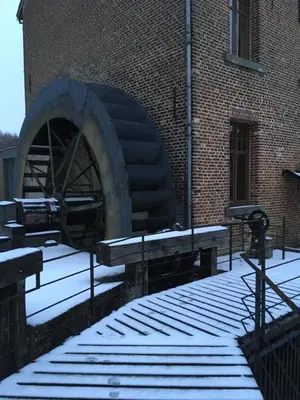 a snow covered building with a watermill in front of it at De Ruttermolen in Tongeren