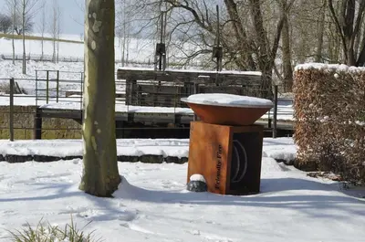 a bird bath sitting in the snow next to a tree at De Ruttermolen in Tongeren
