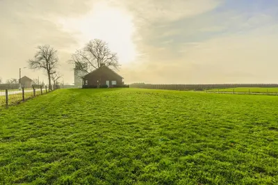 a large green field with a barn in the distance at De Oude Katsei in Gingelom