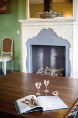a table with two glasses and a book on it with a fireplace at B&B Kamerijck in Gingelom