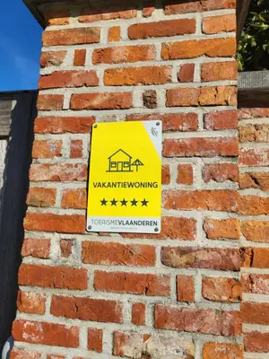 a yellowwarning sign on a brick wall at 'Hof der Heerlijckheid' in Borgloon