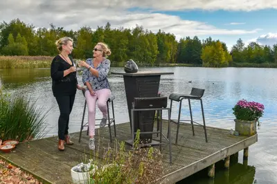 two women sitting on a dock on a lake at Vakantiewoning ‘t Reigersnest in Zonhoven
