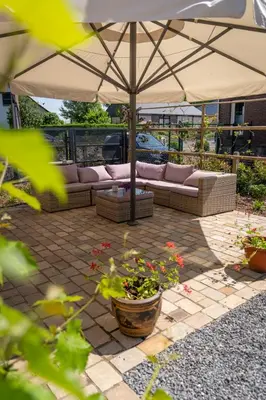 a patio with a couch and an umbrella at Bed & Breakfast 't Vèèrke in Dilsen-Stokkem