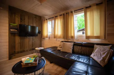 a living room with a leather couch and a television at Chalet de bosuil in Zutendaal