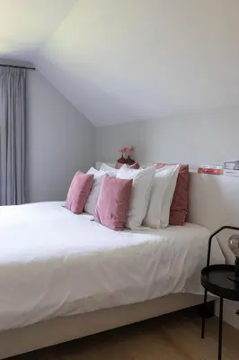 a bedroom with a white bed with pink and white pillows at De Sjieper in Lanaken