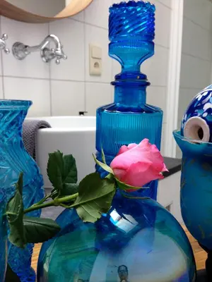 a blue glass vase with a pink rose in it at PuurTeuven B&B tussen Kunst en Natuur in Voeren