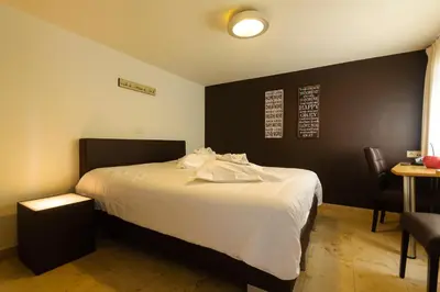 a bedroom with a bed with white sheets and a table at Hotel Pracha in Borgloon