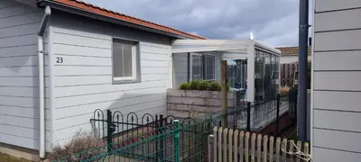 a white house with a porch with a fence at Maas Chalet Aldeneik in Maaseik
