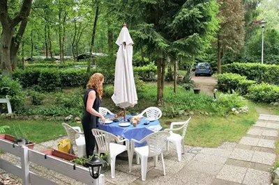 a woman standing next to a table with a umbrella at Nieuw vebouwd Vakantie Boshuisje Meibloempje in Lanaken