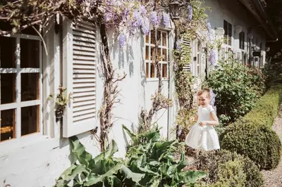 a little girl in a white dress standing outside a building at de Bosch in Lummen