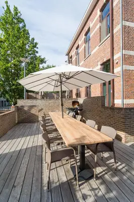 a wooden table with chairs and an umbrella on a deck at Het Dorpshuys - vakantiewoning tot 12 personen in Maaseik