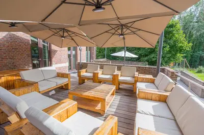 a patio with chairs and tables and an umbrella at Het Dorpshuys - vakantiewoning tot 12 personen in Maaseik