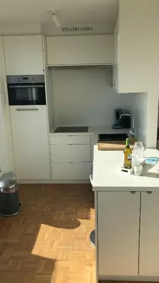 a kitchen with white cabinets and a wooden floor at Gezellig 1 slaapkamer appartement nabij het stadscentrum in Hasselt