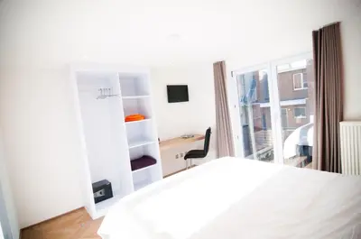 a bedroom with a bed and a desk and a window at Apartment De Maasnacht in Maaseik