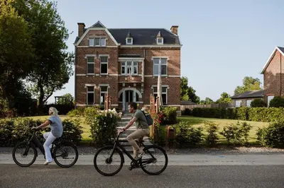 two people riding bikes in front of a house at B&B het Notarishuis - authentiek verblijf nabij Maastricht in Voeren