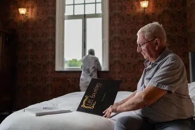 an older man sitting on a bed with a book at Villa les Bruyères in Dilsen-Stokkem