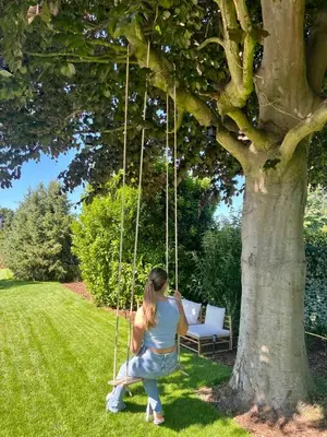 a woman sitting on a swing under a tree at Vakantiewoning De Winning in Houthalen-Helchteren