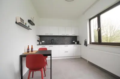 a kitchen with white cabinets and a table and red chairs at Oscappart in Eupen